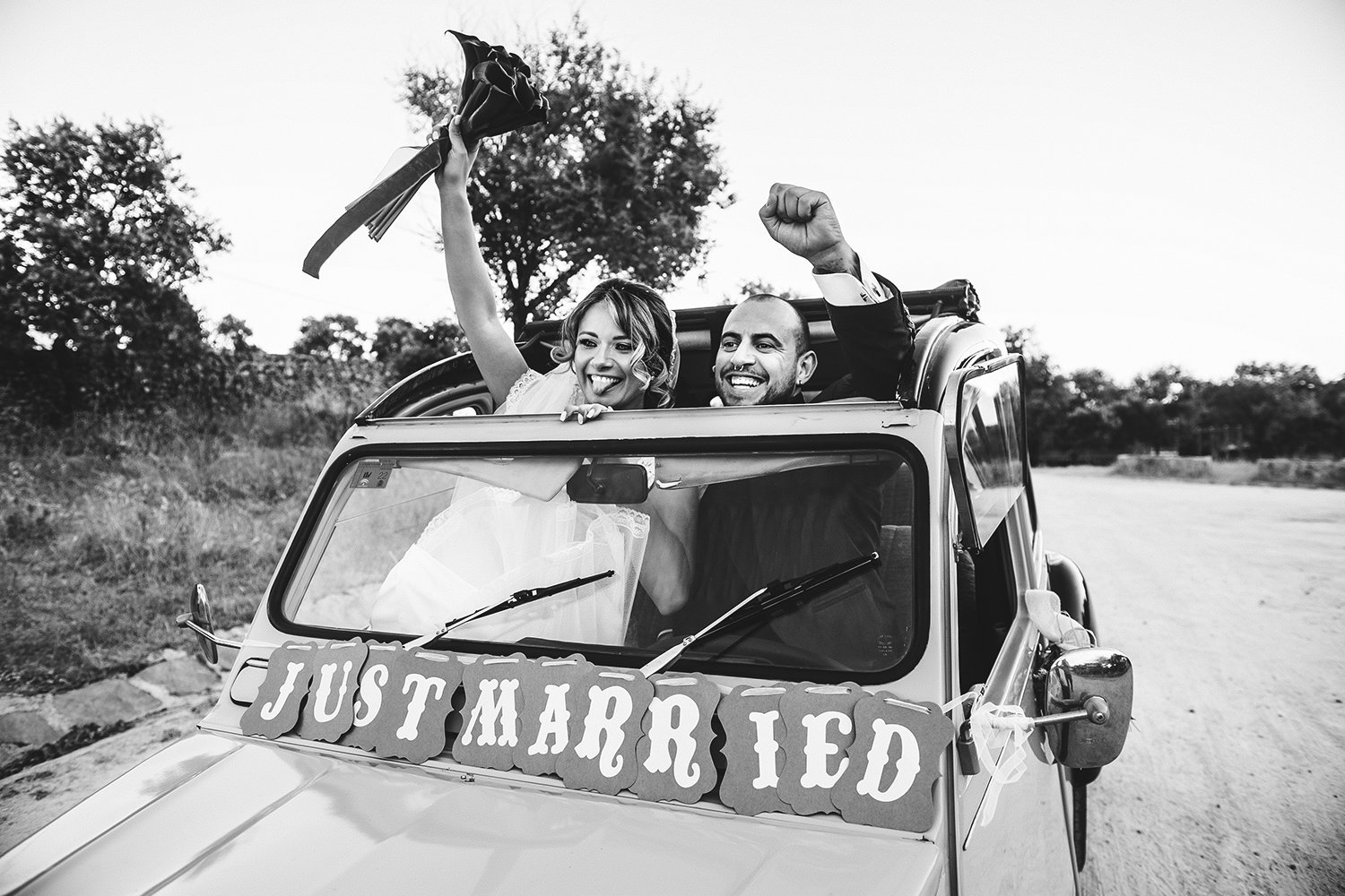 Jara y Juanjo celebran su boda levantando los brazos desde un coche clásico con un cartel de Just Married.