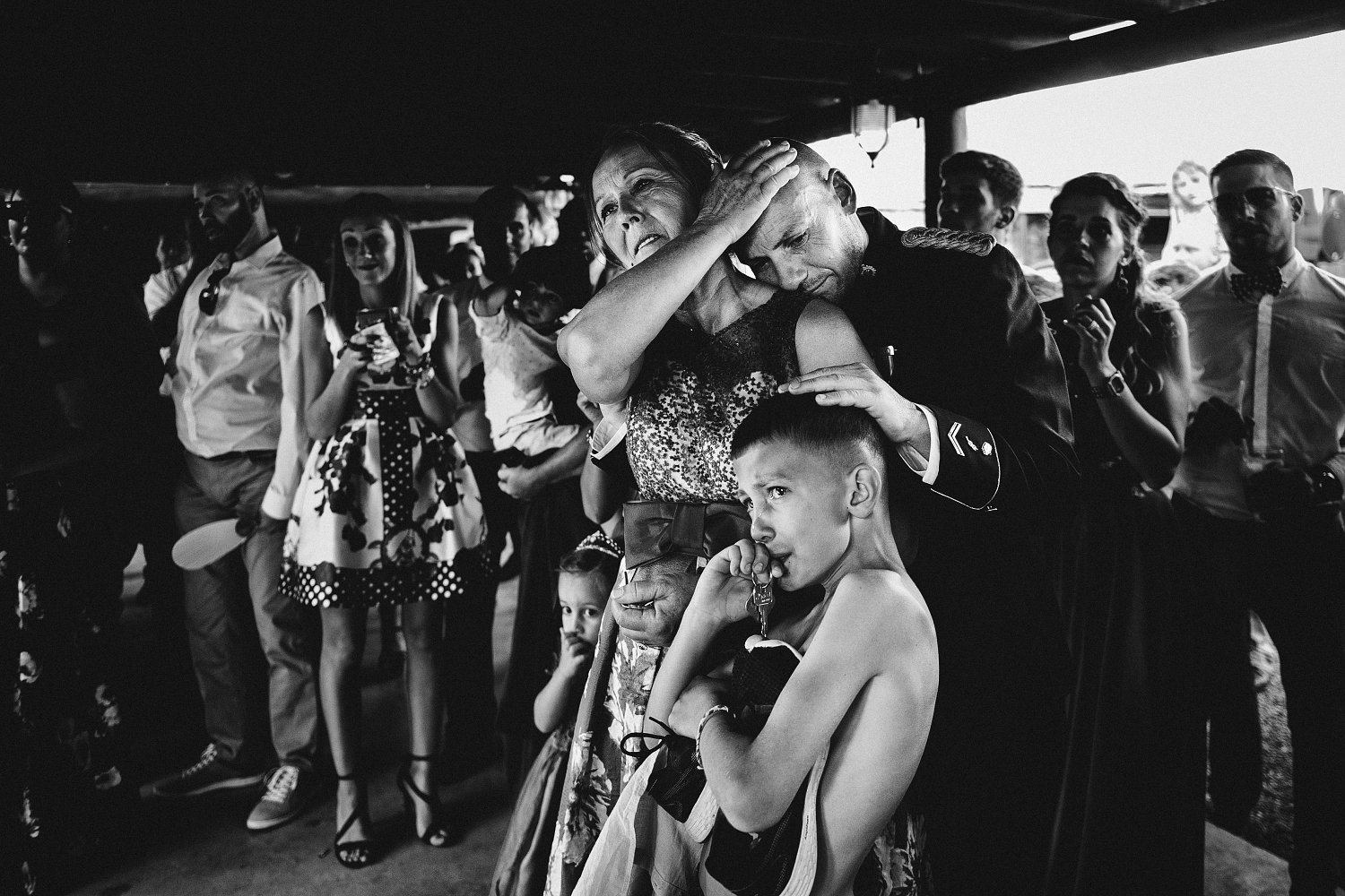 Hombre emocionado abrazando a una mujer mientras acaricia la cabeza de un niño, rodeados de invitados durante una boda en Fuerteventura.