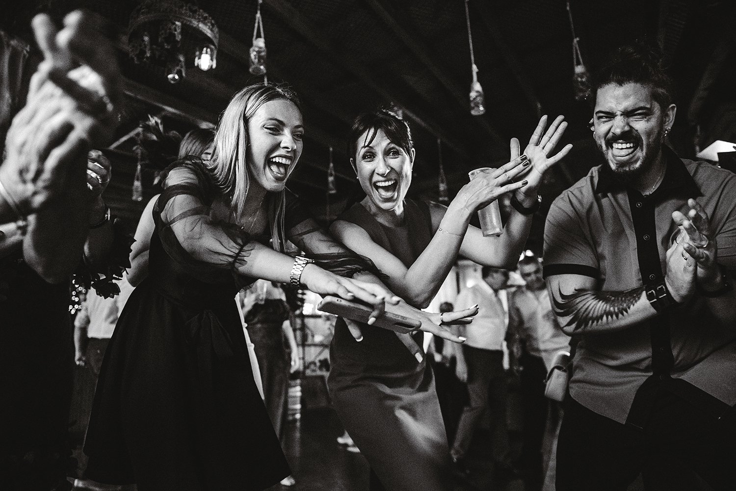 Tres invitados riendo y bailando durante una fiesta de boda en Valencia, fotografiados en blanco y negro.