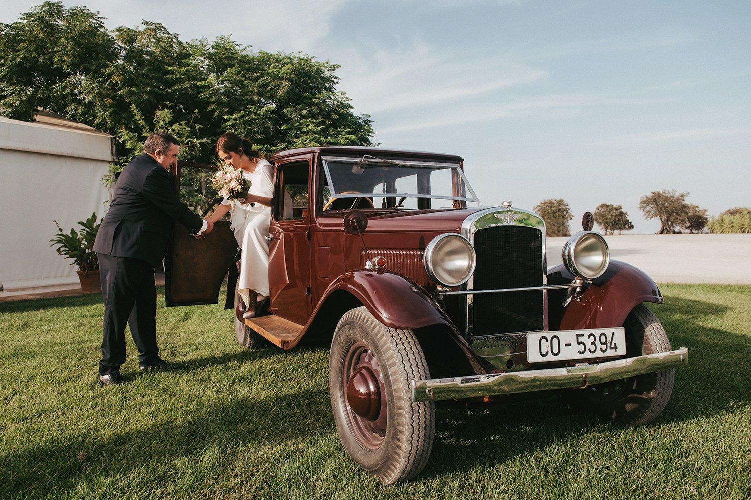 Nuria bajando de un coche clásico acompañada por su padre el día de su boda en Extremadura